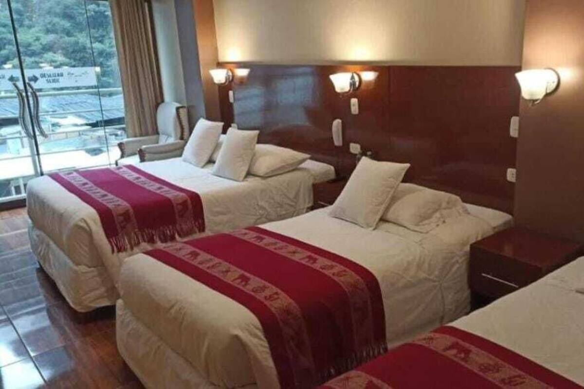 Una habitación de hotel con dos camas, un ventanal grande y un cabecero de madera.