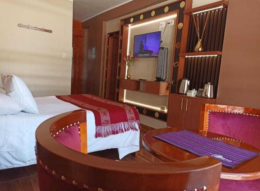 A hotel room with a bed, a wooden armchair, a small table, a TV, and a minibar.
