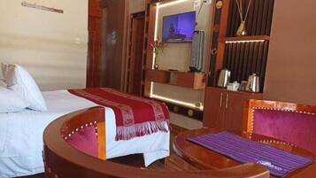 A hotel room with a bed, a wooden armchair, a small table, a TV, and a minibar.
