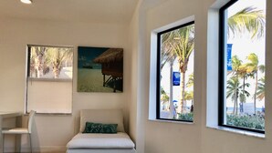 Una stanza con piscina, una sedia, un divano con cuscino con la scritta 'hello' e vista sulla spiaggia dalle finestre.