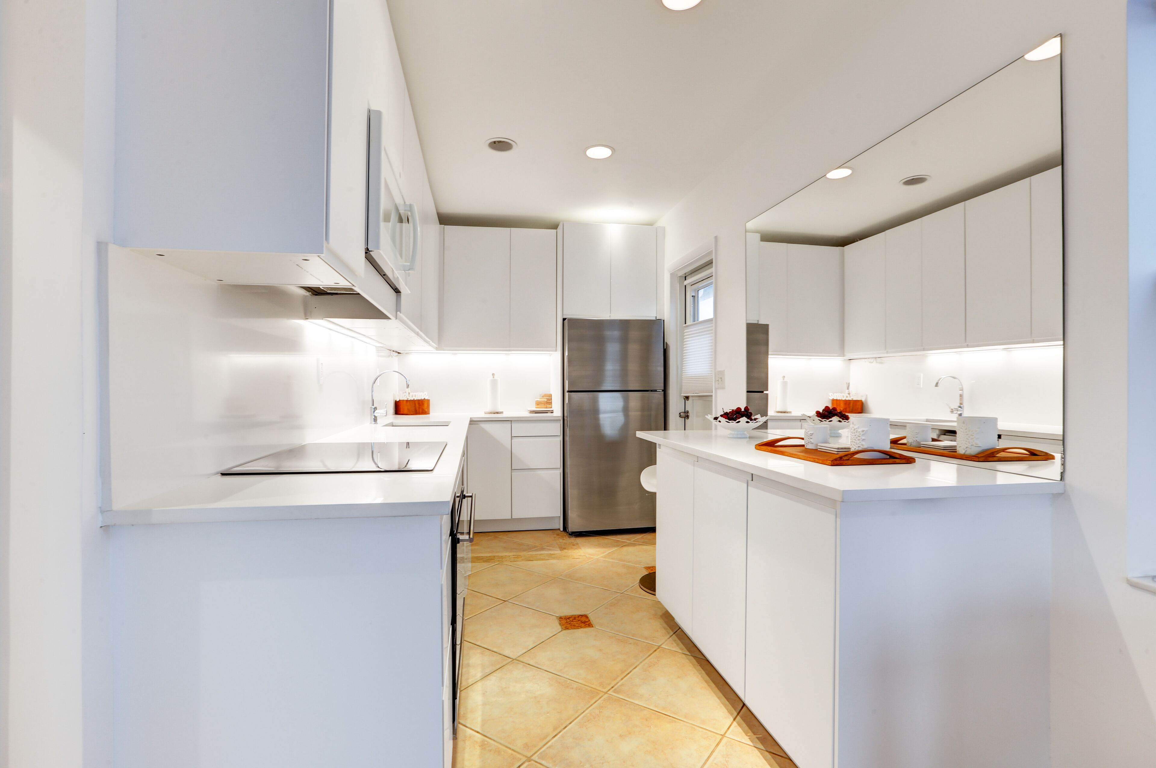 Una cocina moderna con armarios blancos, electrodomésticos de acero inoxidable y piso de baldosas.