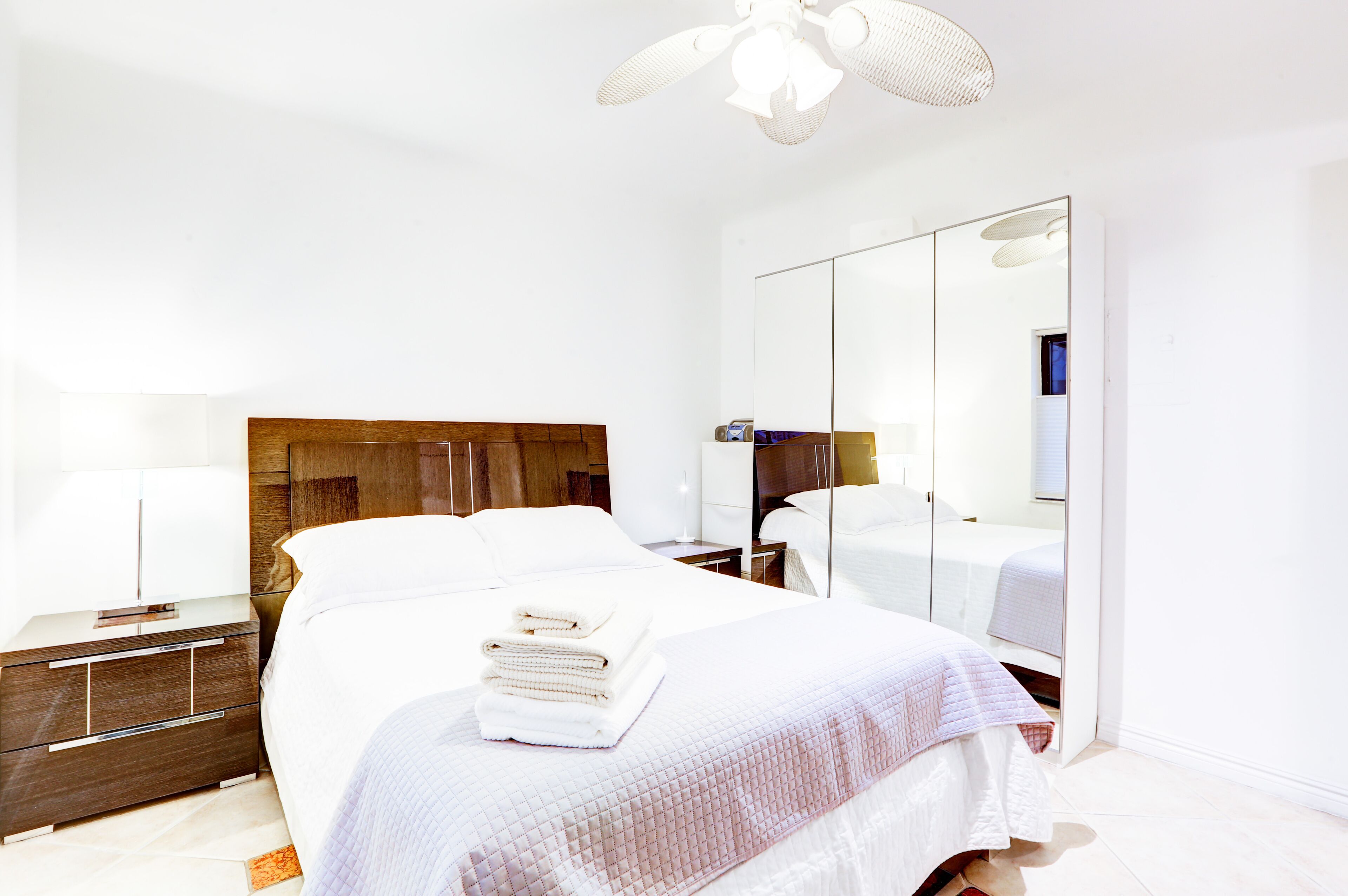 A hotel room with a large bed, a wooden headboard, a nightstand with a lamp, a mirror, and a wardrobe.