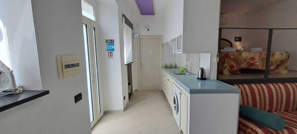 A compact kitchen with a washing machine, a coffee maker, and a striped sofa in the living area. - Tauto Apartment ..... (Atrani)