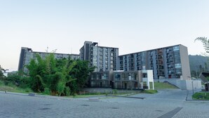 Un bâtiment moderne à plusieurs étages, doté d’un toit plat, de grandes fenêtres et d’un espace paysager agrémenté d’arbres.