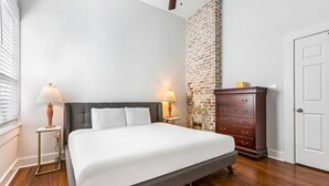 A neatly arranged bedroom with a large bed, two bedside lamps, a dresser, and a brick accent wall. - 15% OFF Monthly | 10% OFF Weekly-Spacious 5BR Near Magazine St & Uptown (New Orleans)