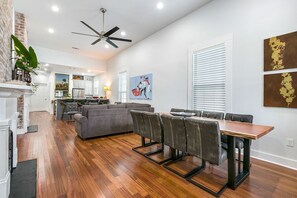 Une cuisine moderne avec des meubles blancs, un coin repas avec une table et des chaises en bois, et un salon avec un canapé gris et une cheminée.