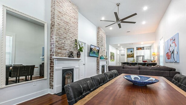 A spacious living room with a long wooden dining table, black leather sofas, a fireplace, and a ceiling fan. - 15% OFF Monthly | 10% OFF Weekly-Spacious 5BR Near Magazine St & Uptown (New Orleans)
