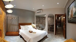 Ein Hotelzimmer mit Backsteinwand, einem Bett mit weißen Leinentüchern, einem runden Spiegel und einem Bild an der Wand.