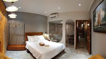 Une chambre d’hôtel avec un mur en briques, un lit recouvert de draps blancs, un miroir rond et un tableau accroché au mur.