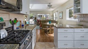 A spacious kitchen with a gas stove, white cabinets, and a dining area with a table and chairs. - 8th Avenue Beach Cottage (Santa Cruz)