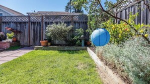 A backyard with a wooden fence, potted plants, and a blue paper lantern. - 8th Avenue Beach Cottage (Santa Cruz)