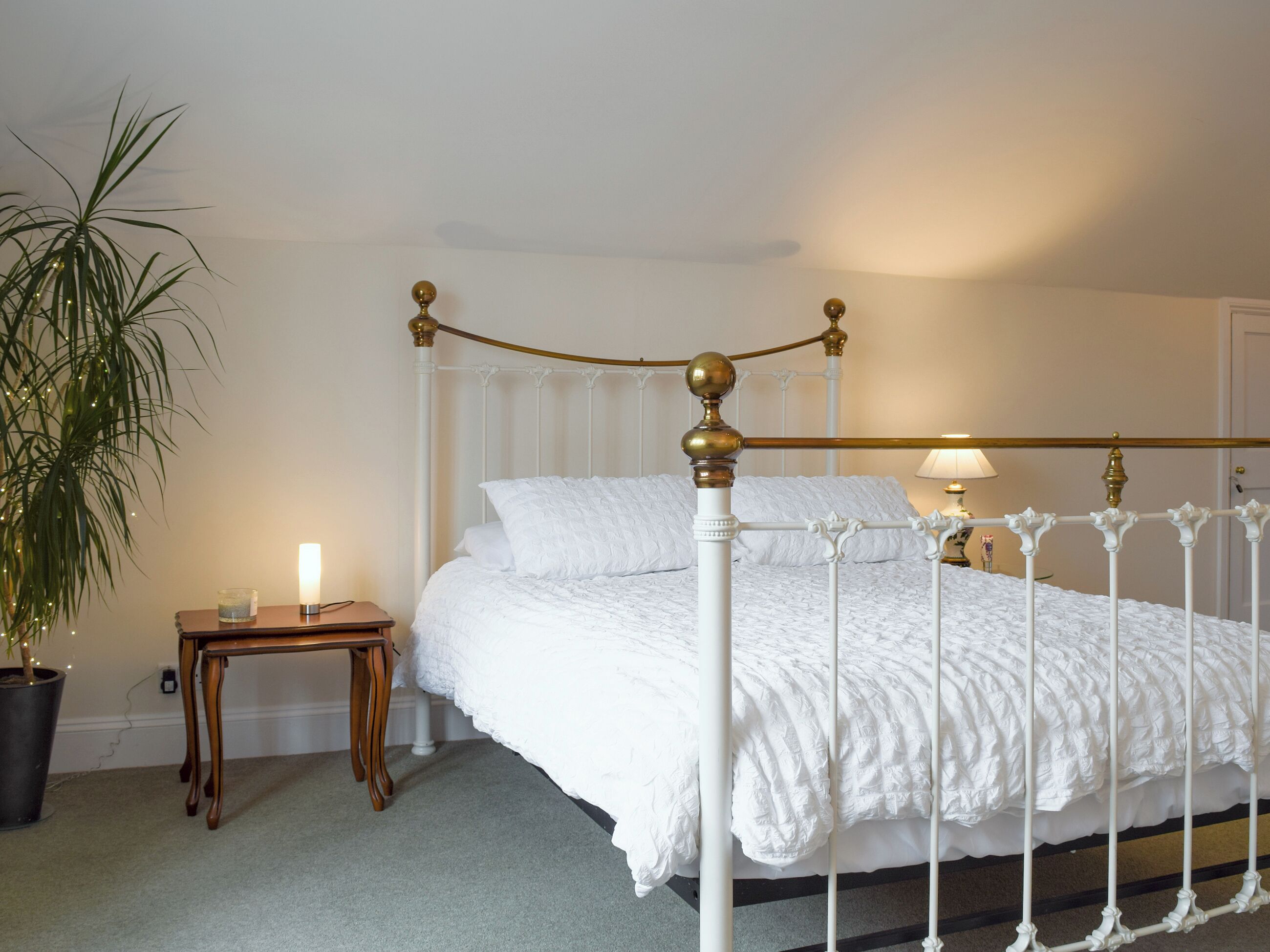 Un lit bien fait, avec une couette blanche et des oreillers, une table de chevet avec une lampe et une plante en pot.