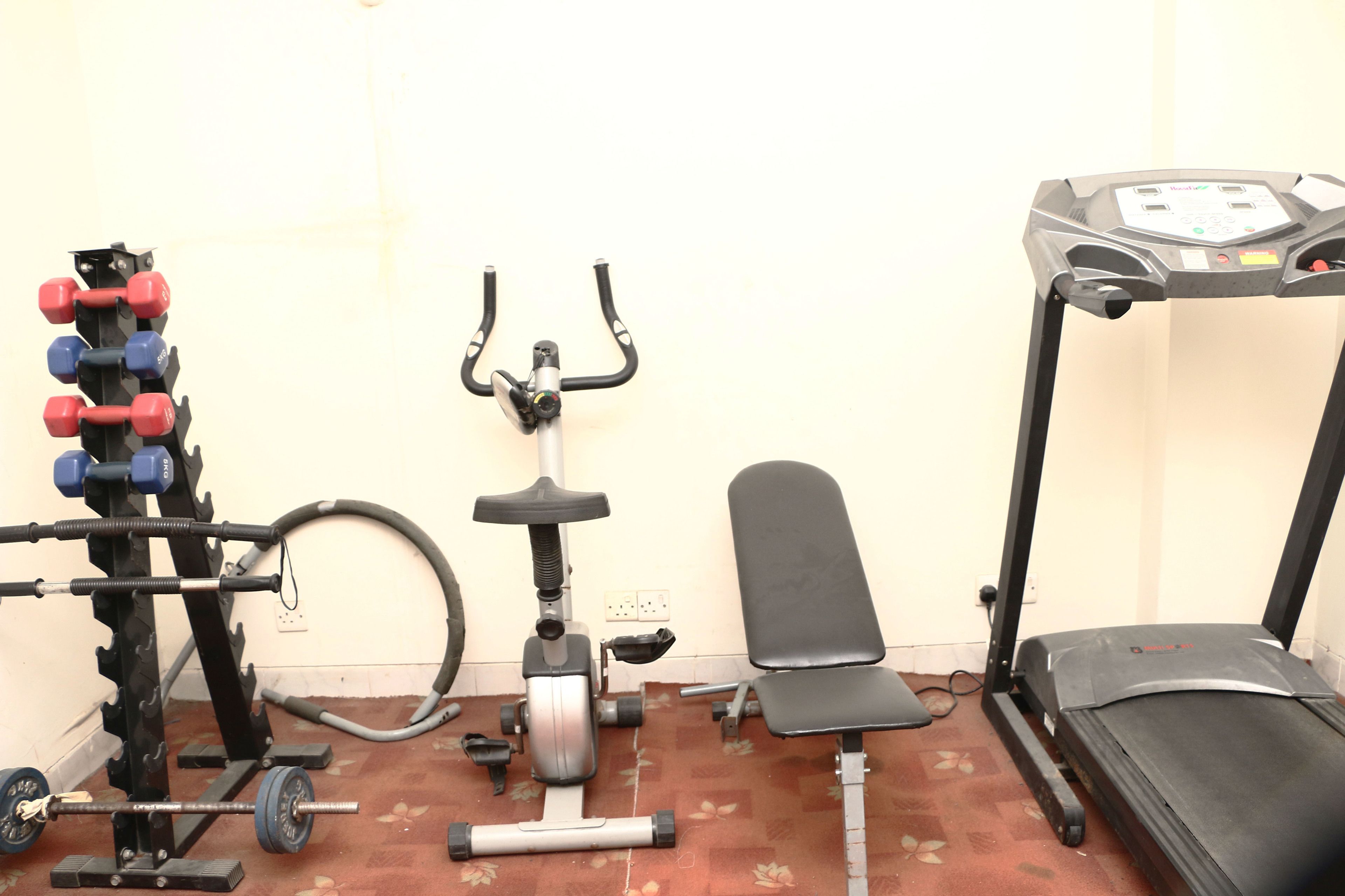 A home gym with a barbell rack, dumbbells, an elliptical, a bench, and a treadmill.