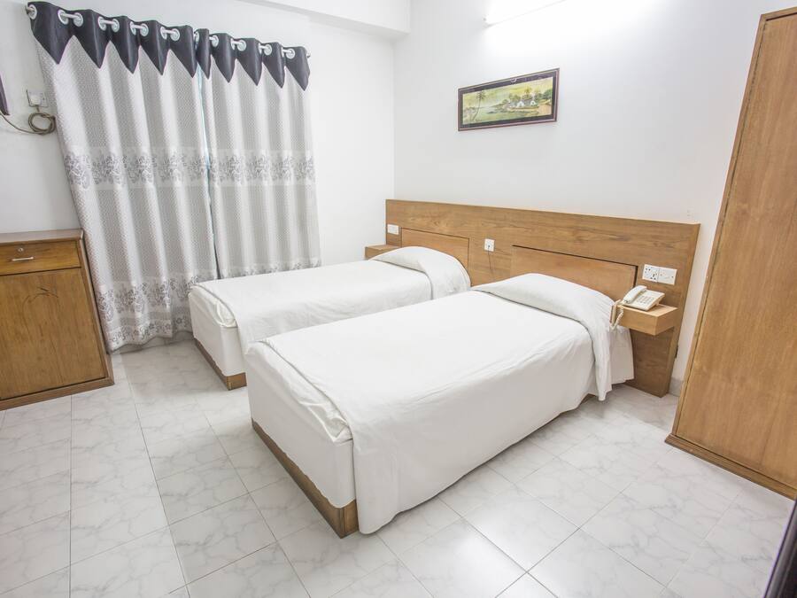 A hotel room with two beds, a wooden headboard, a nightstand with a telephone, a wooden wardrobe, and a window with a curtain.