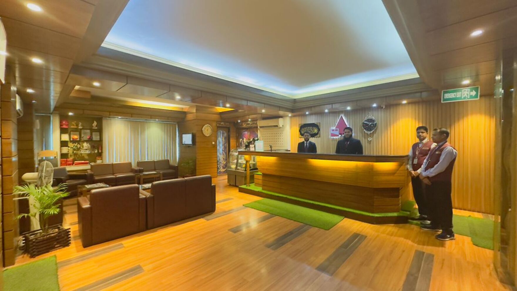 Ein Hotel-Empfangsbereich mit einem Holzbüro, Ledersitzmöbeln und einem grünen Teppich.