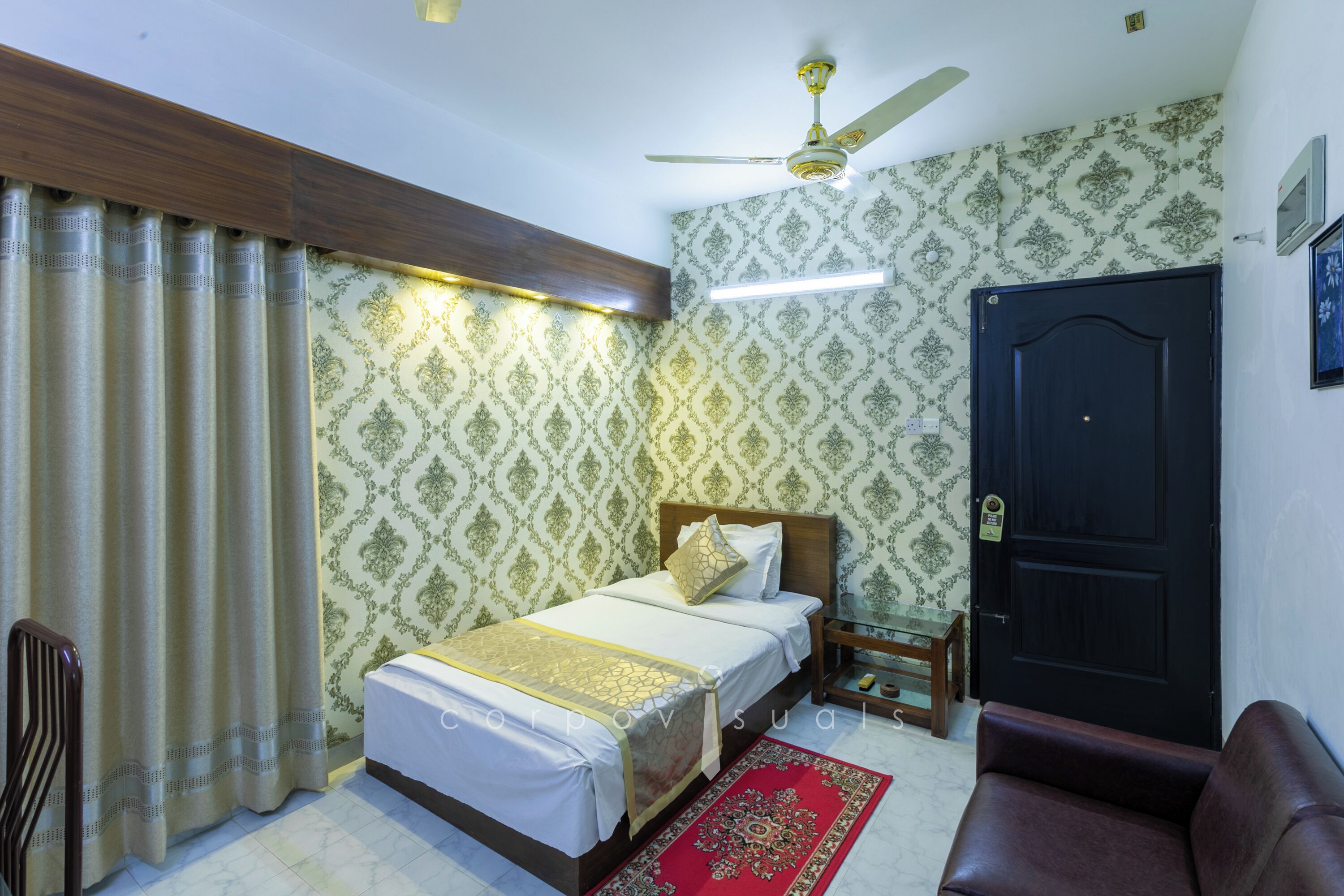 A bedroom with a bed, a wooden headboard, a nightstand, a red rug, a ceiling fan, and a black door.