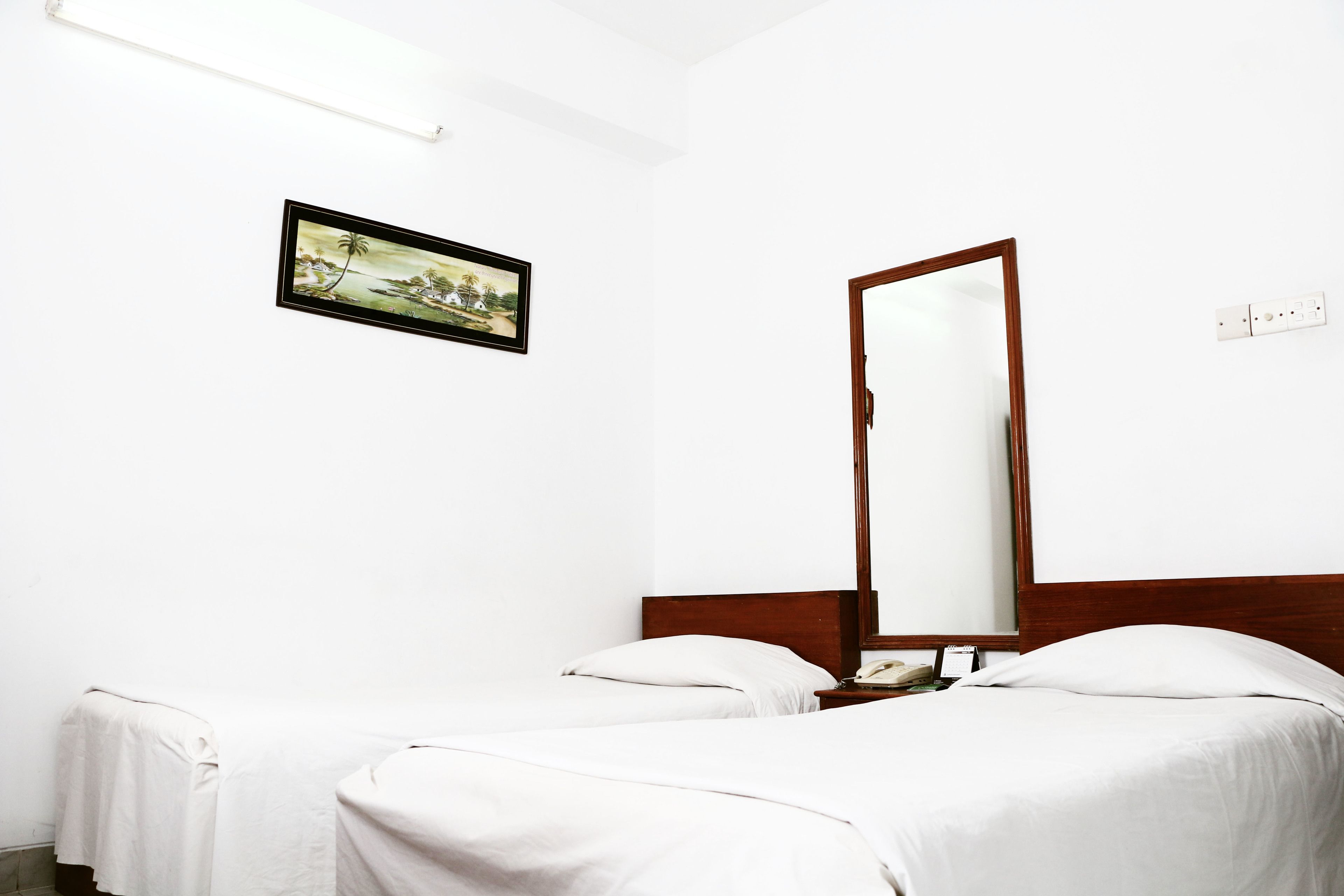 Een hotelkamer met twee eenpersoonsbedden, een houten hoofdbord, een nachtkastje met een lamp, een ingelijst schilderij aan de muur, en een spiegel.