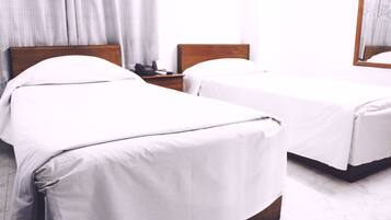 A hotel room with two single beds, a wooden headboard, a bedside table with a phone, and a large mirror on the wall.