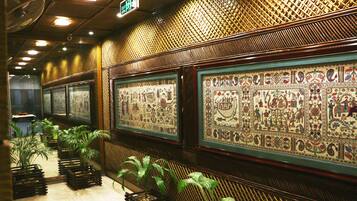 A hallway with framed artwork on the walls, potted plants, and a patterned ceiling.