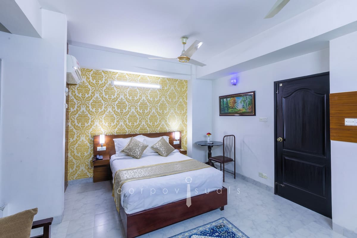 Un dormitorio con cama, mesitas de noche, ventilador de techo, una puerta y una pequeña mesa con silla.