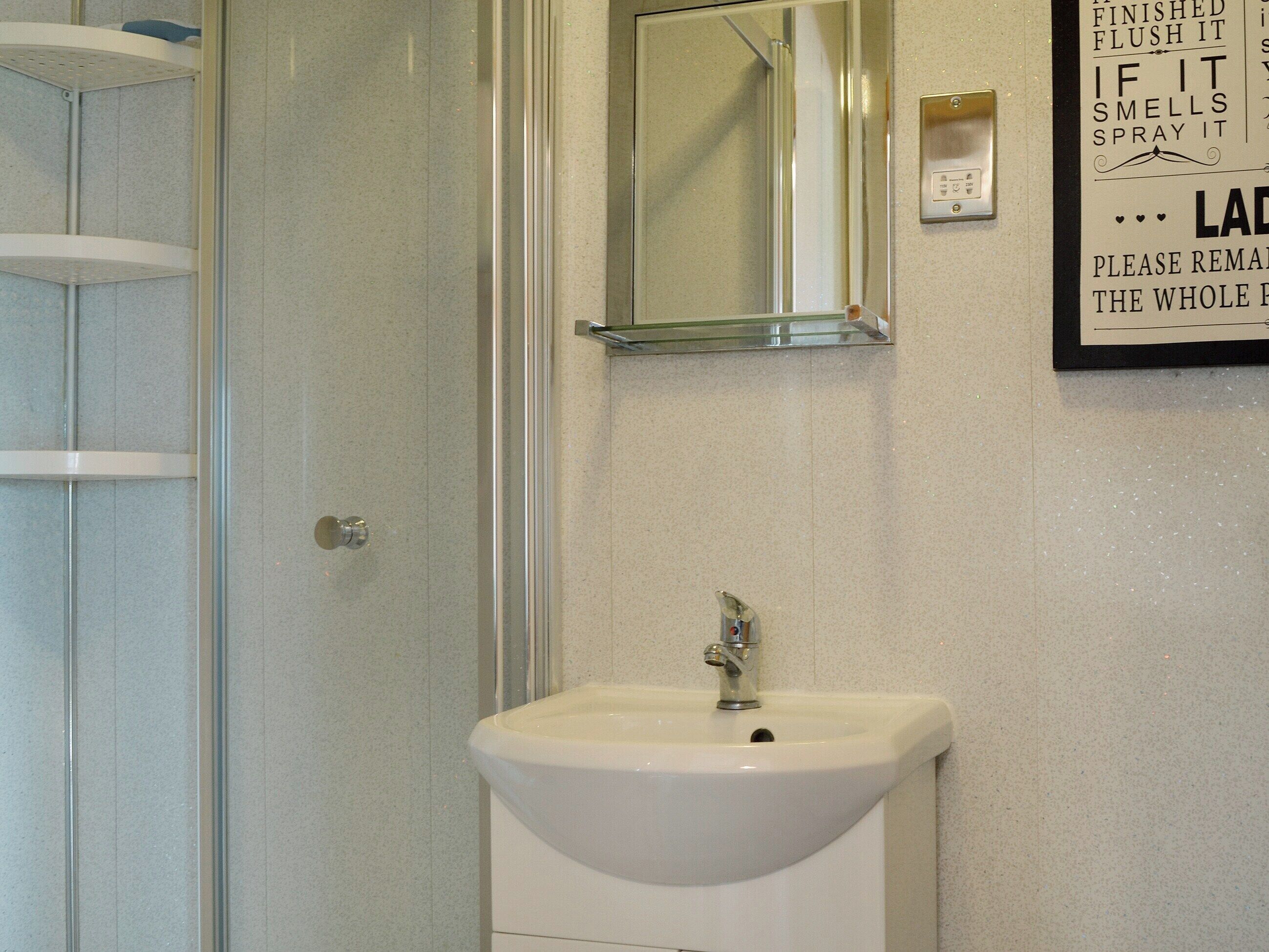 A bathroom with a white sink, a mirror, and a wall-mounted light switch.