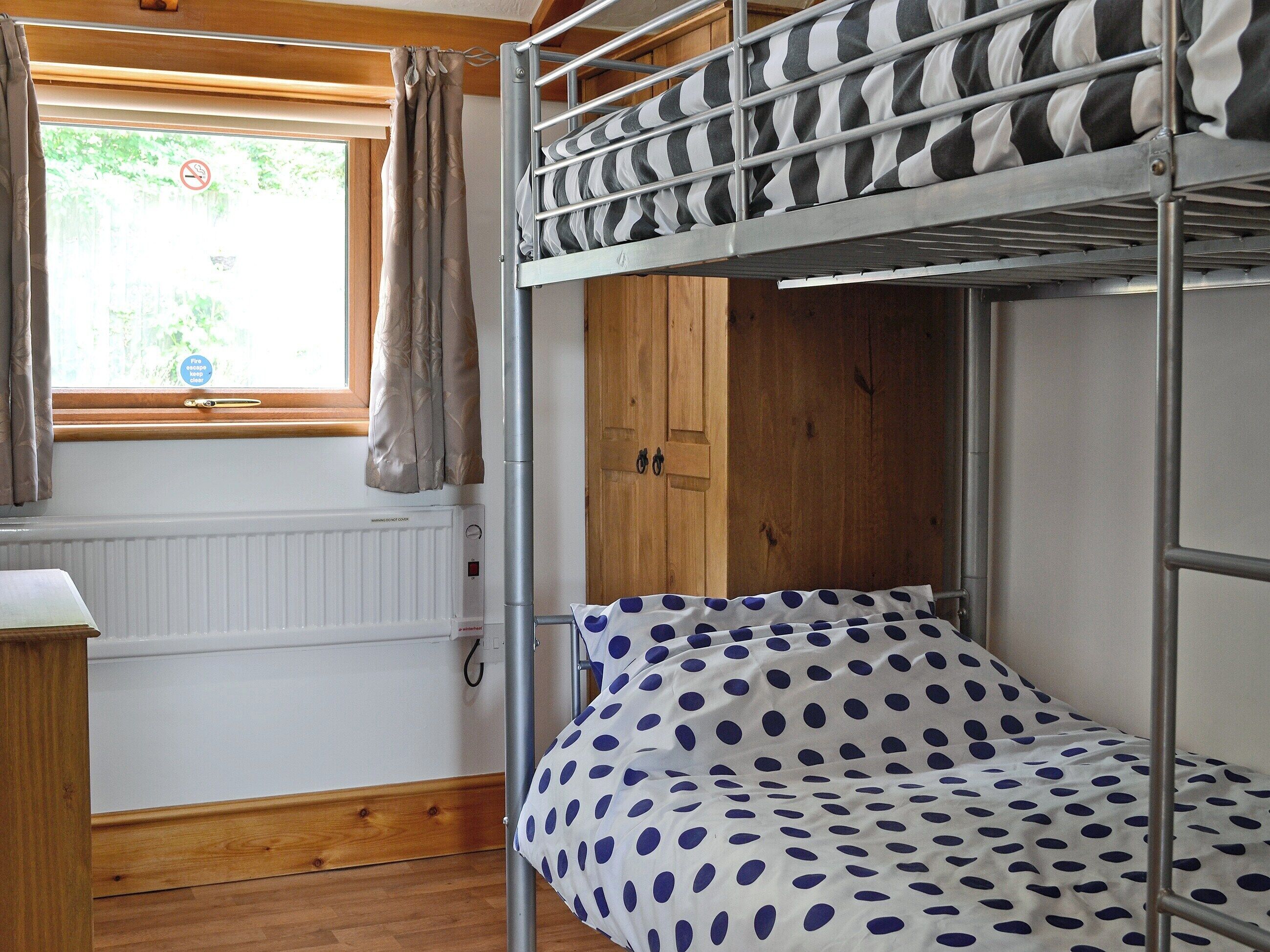 Een slaapkamer met stapelbed, raam, gordijnen, een radiator en een houten deur.