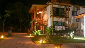 A modern building with a wooden staircase leading to a balcony, surrounded by well-lit garden areas. - Pousada Maré (Prado)