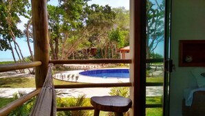 A hammock on a wooden deck with a view of a pool and beach. - Pousada Maré (Prado)