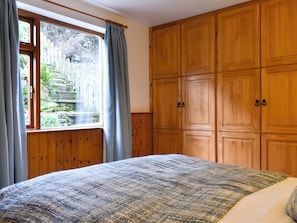 A bedroom with a large bed, wooden wardrobe, and a window with curtains.