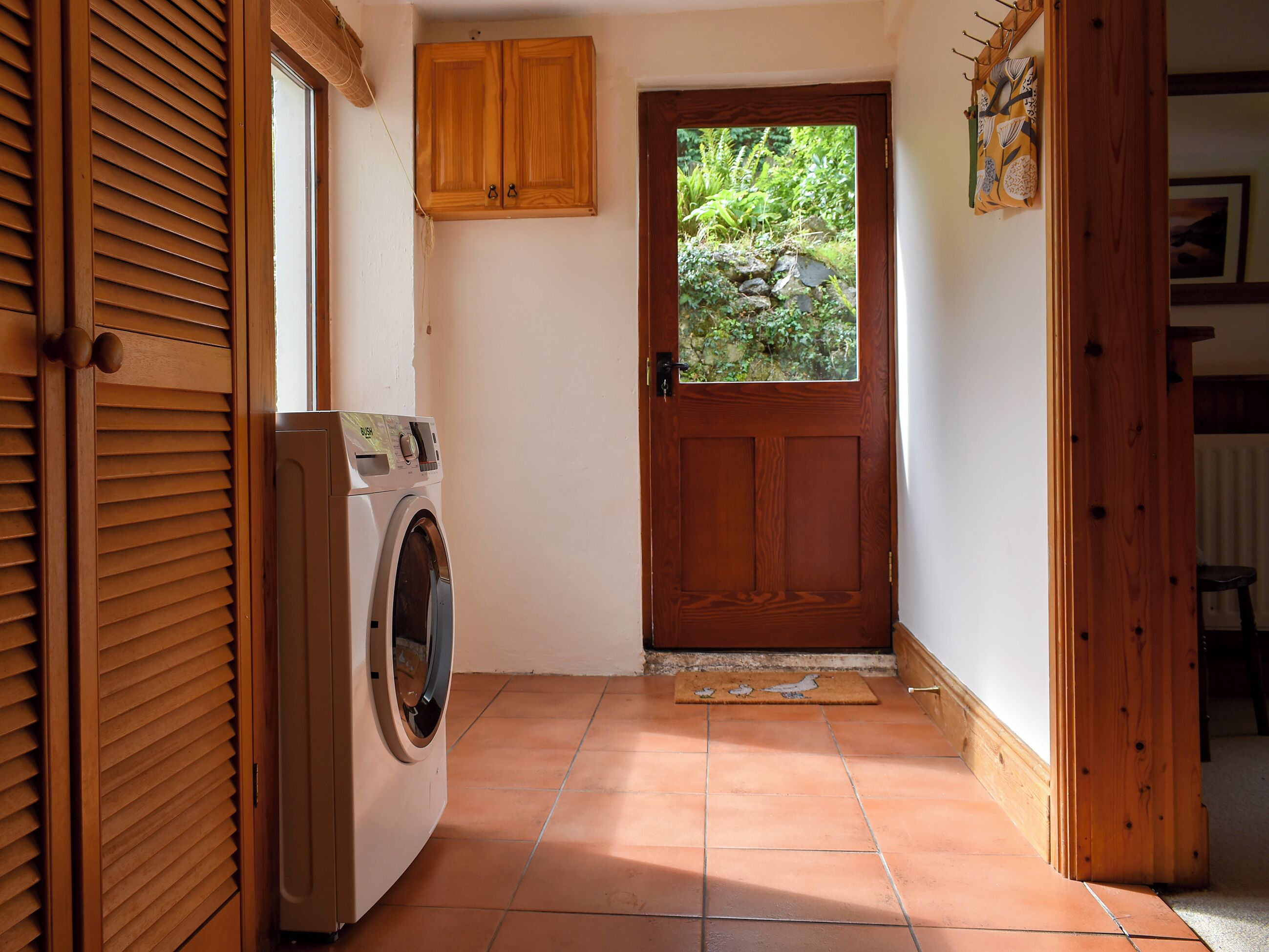 A laundry room with a washing machine, wooden cabinets, and a door leading to a garden.