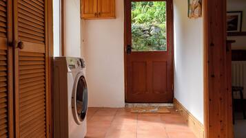 A laundry room with a washing machine, wooden cabinets, and a door leading to a garden.