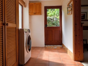 A laundry room with a washing machine, wooden cabinets, and a door leading to a garden.