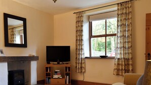 A living room with a fireplace, a television, a bookshelf, and a window with curtains. - 1 bedroom accommodation in Lindale, near Grange-over-Sands (Lindale, near Grange-over-Sands)