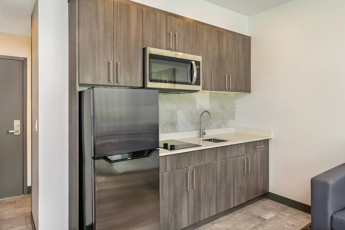 A kitchen with a stainless steel refrigerator, a microwave, and wooden cabinets.