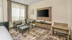 Habitación de hotel con cama, escritorio, silla, televisión y un banco.
