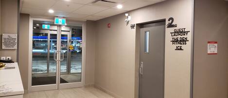 A hotel corridor with a glass door entrance, a sign for the second floor, and a wall-mounted sign indicating guest laundry, the Den, and ice facilities.