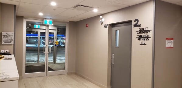A hotel corridor with a glass door entrance, a sign for the second floor, and a wall-mounted sign indicating guest laundry, the Den, and ice facilities.