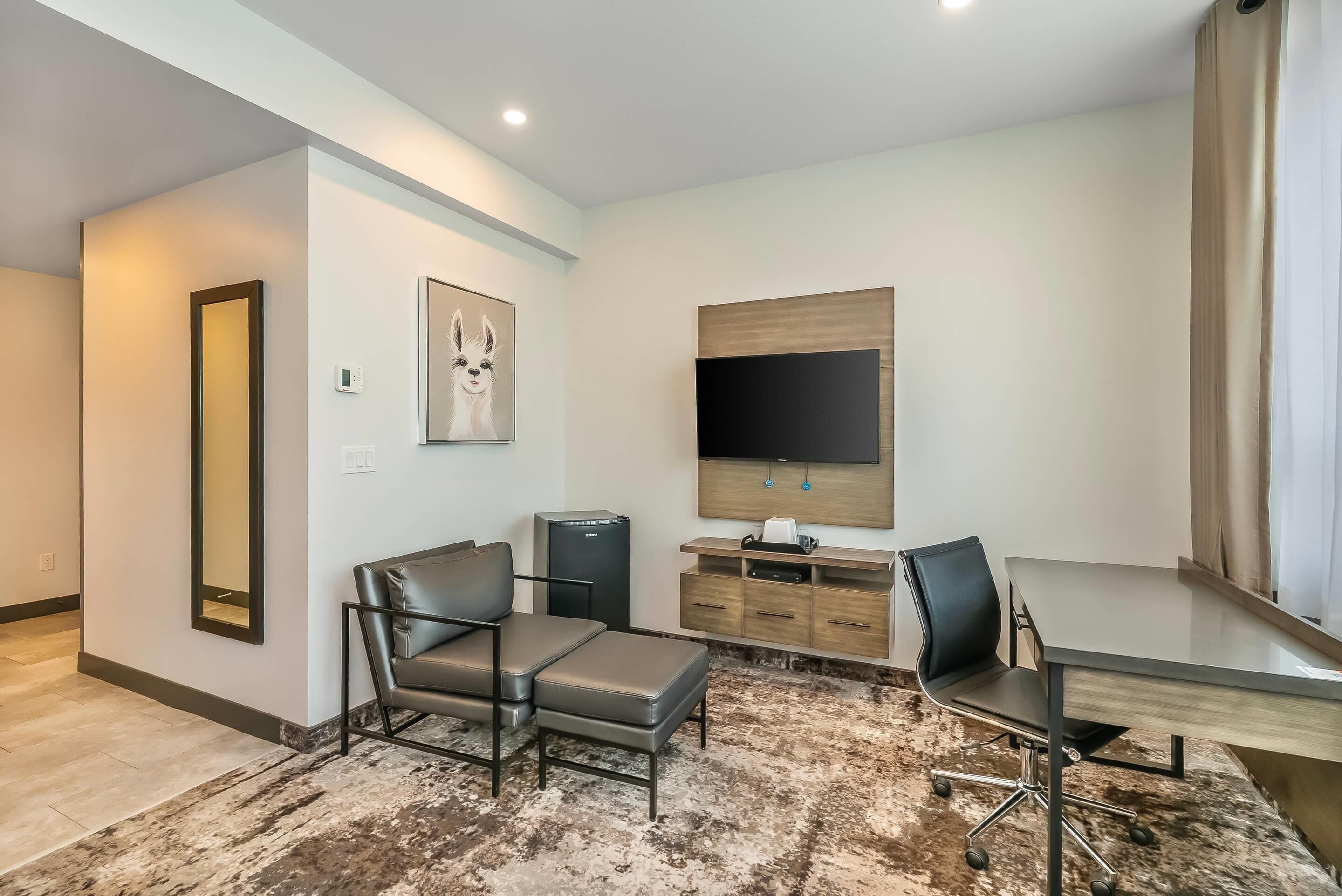 A modern hotel room with a sofa, a desk, a TV, a mirror, and a wooden cabinet.