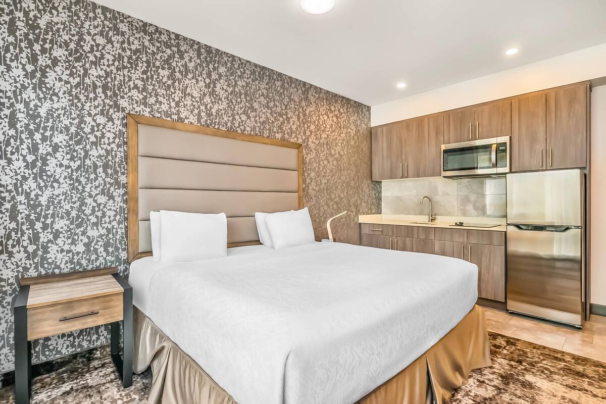 A hotel room with a large bed, a nightstand, a wooden cabinet, a microwave, and a refrigerator.
