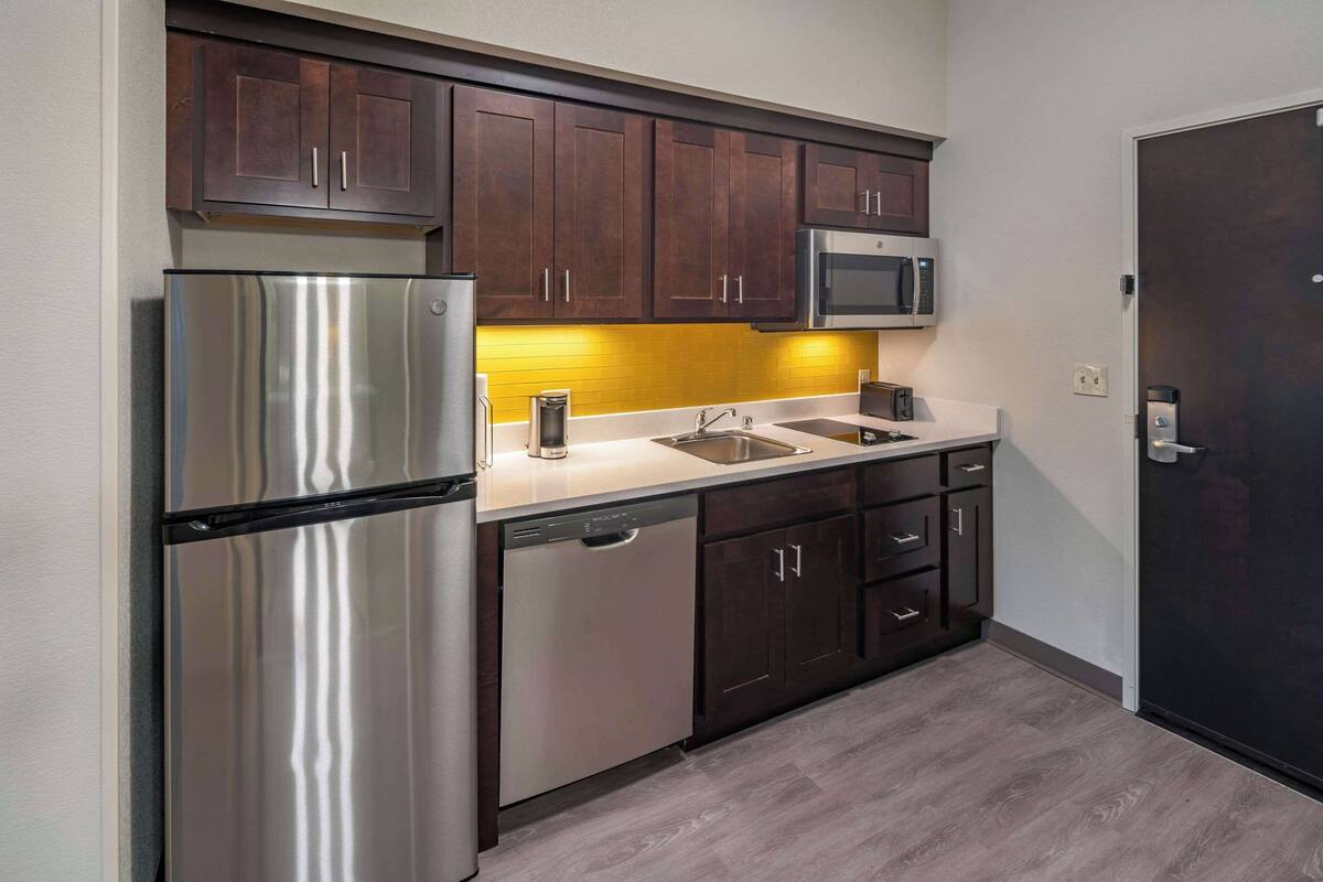 A compact kitchen with dark wooden cabinets, stainless steel appliances, and a yellow backsplash.