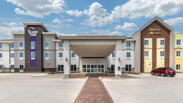 A hotel with a central entrance, Sleep Inn and MainStay Suites signs, and a clear sky. - MainStay Suites Spokane Airport (Spokane)