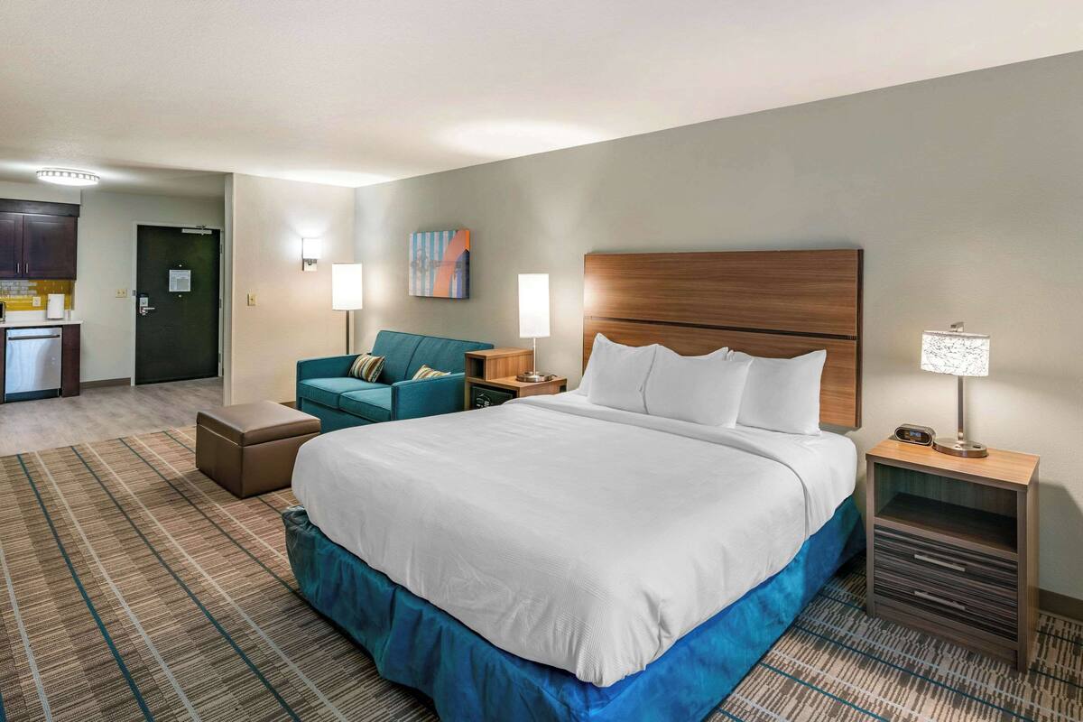 A hotel room with a large bed, a sofa, a desk, and a kitchenette.