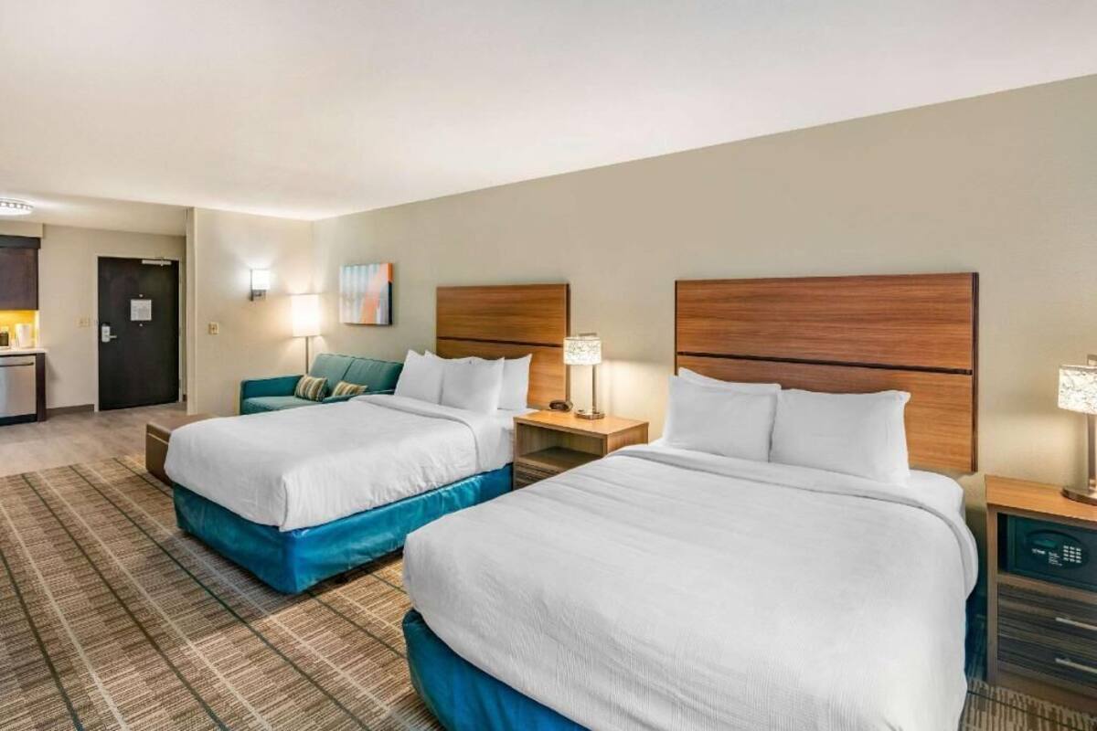 A hotel room with two beds, a desk, a chair, a lamp, and a wall-mounted artwork.