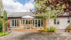 Een huis met een terras, een tafel met stoelen en een grote parasol.