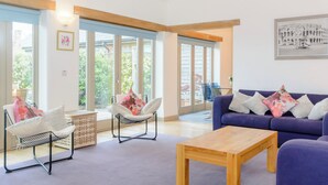 Een moderne woonkamer met een bank, fauteuils, een salontafel en grote ramen.