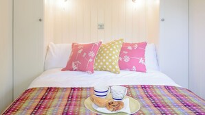 Un lit avec une literie blanche, des coussins colorés et une couverture à motifs arc-en-ciel.