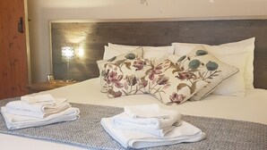Un lit bien fait, agrémenté de coussins à motifs floraux, d’une lampe de chevet et d’une pile d’essuie-main posée sur un chemin de lit texturé.