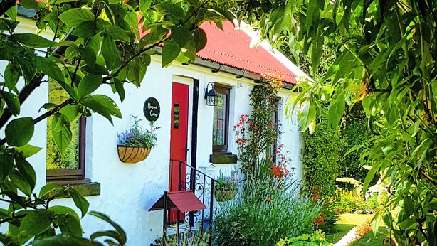 Un bâtiment blanc avec une porte rouge, entouré d’une végétation luxuriante et d’un jardin bien entretenu.