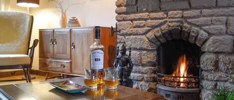 Een gezellige woonkamer met een stenen open haard, een houten kast en een tafel met glazen en een fles.