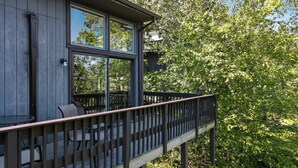 A wooden deck with outdoor seating and large windows overlooking a lush green area.